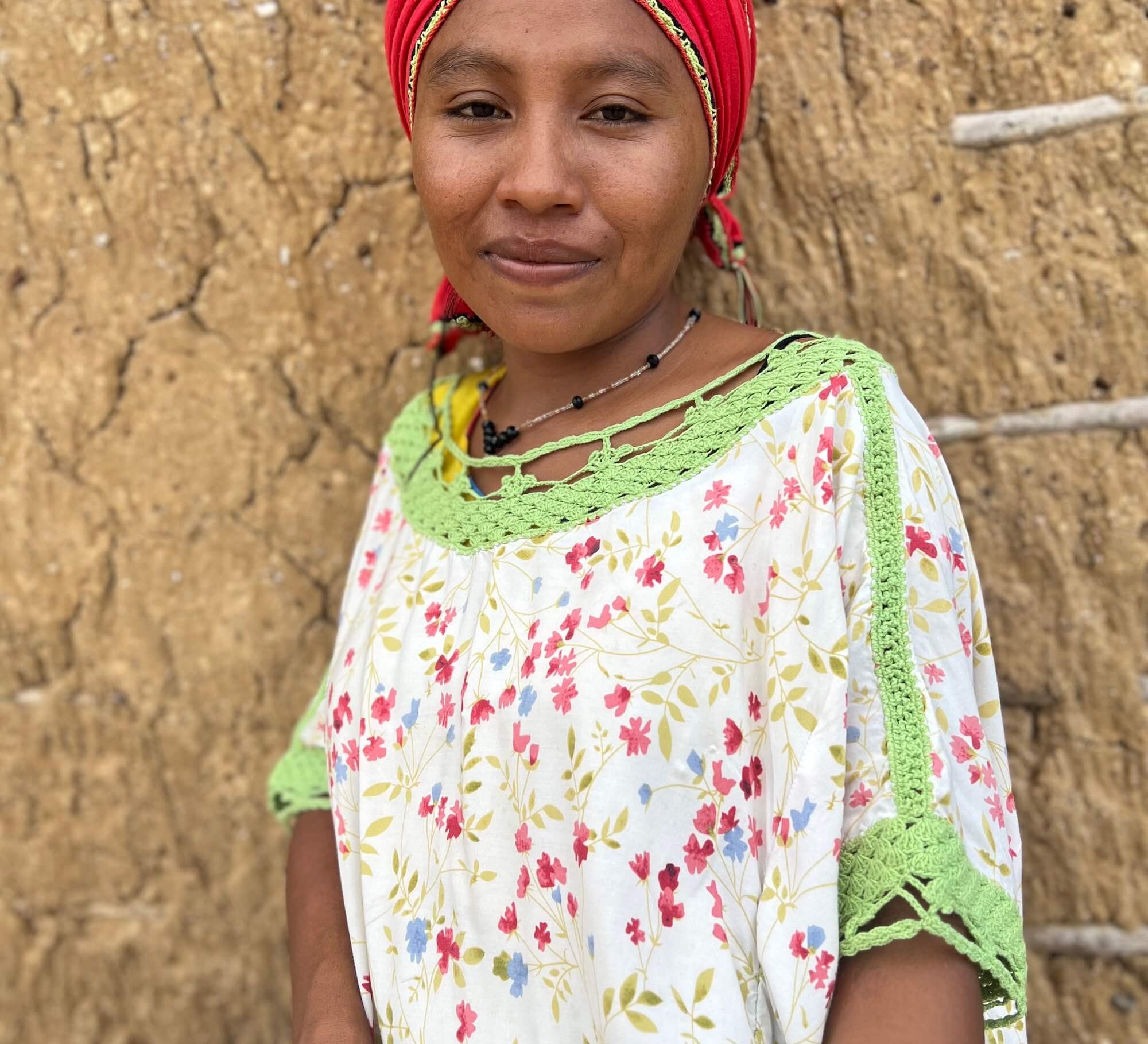 Wayuu woman in colourful "manta" dress and headscarf outside a traditional mud house