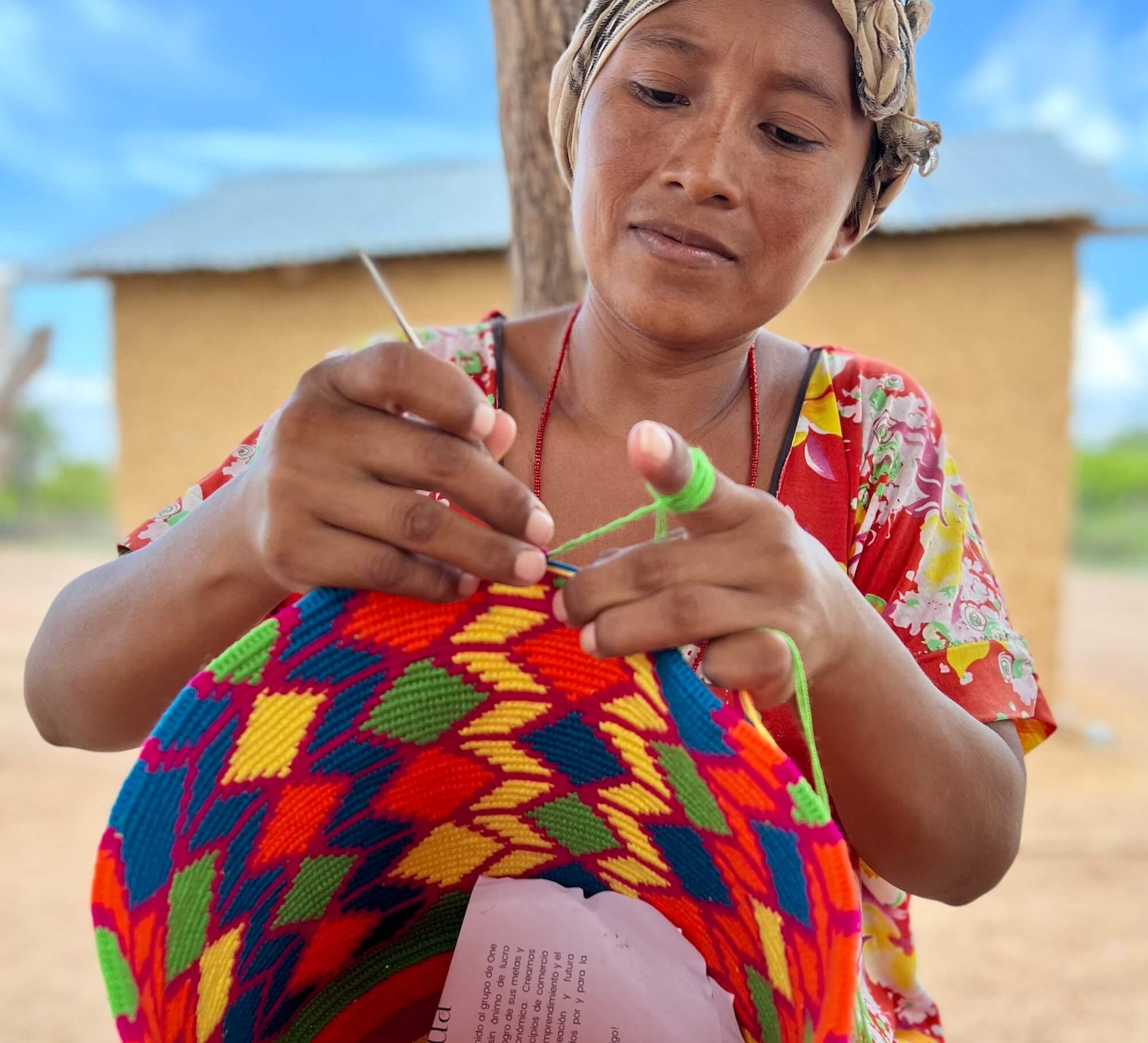 Wayuu woman in a headscarf and bright "manta" dress crocheting a colourful crossbody mochila bag