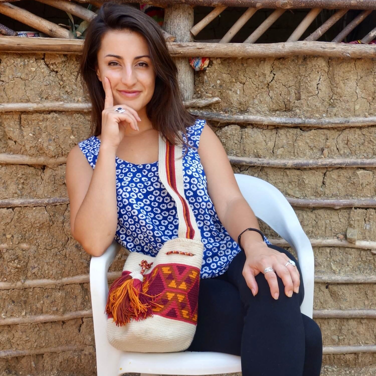 Young women smiling in front of a traditional Wayuu home with a crossbody mochila
