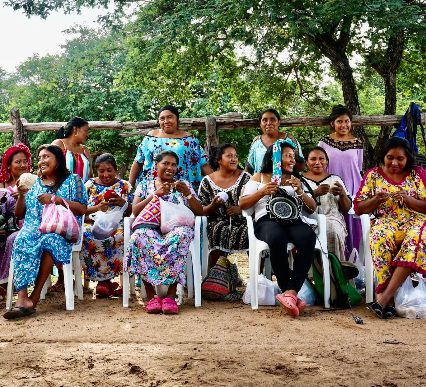 group of Wayuu women sitting and smiling in a rural community crocheting mochilas