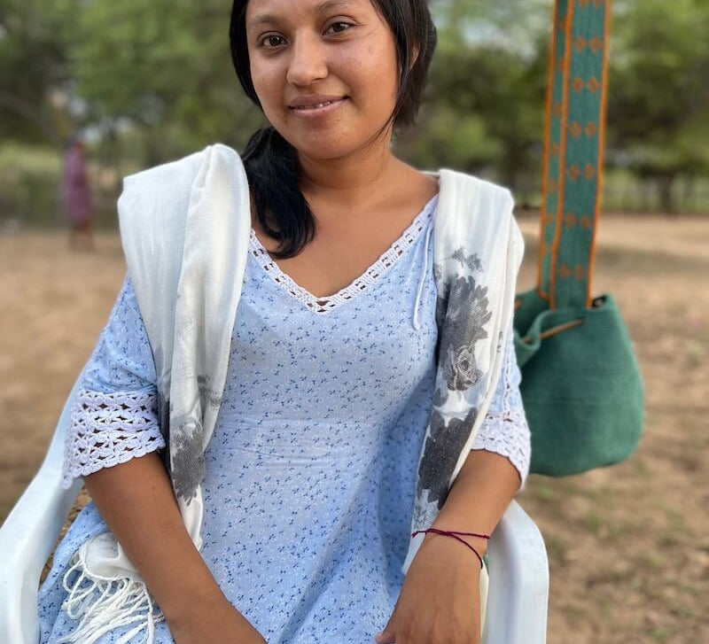 Young Wayuu woman in a blue dress in front of a crossbody mochila bag