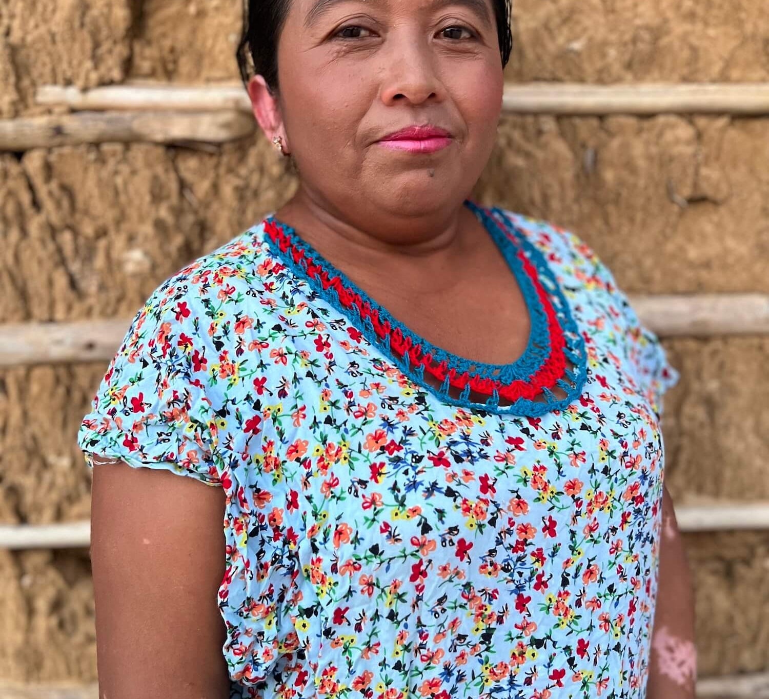 Wayuu woman in colourful "manta" dress in front of a traditional mud and stick house
