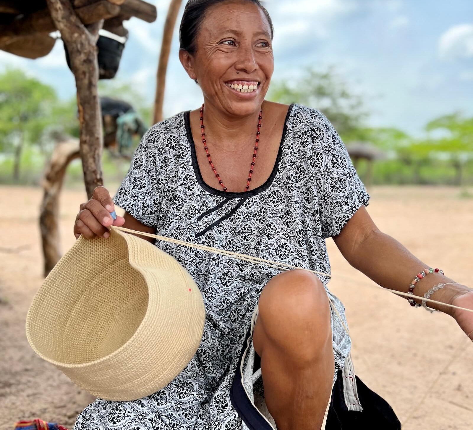 Wayuu woman smiling and crocheting a beige crossbody mochila bag