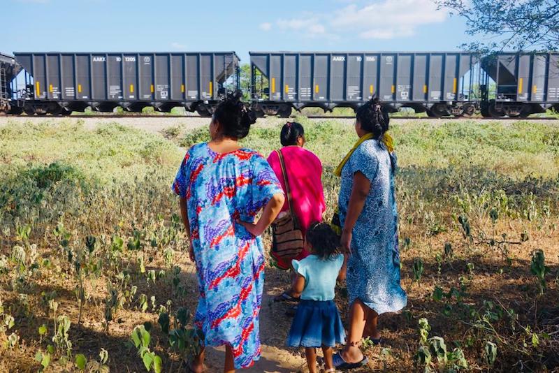 Wayuu women and child standing in front of a coal train