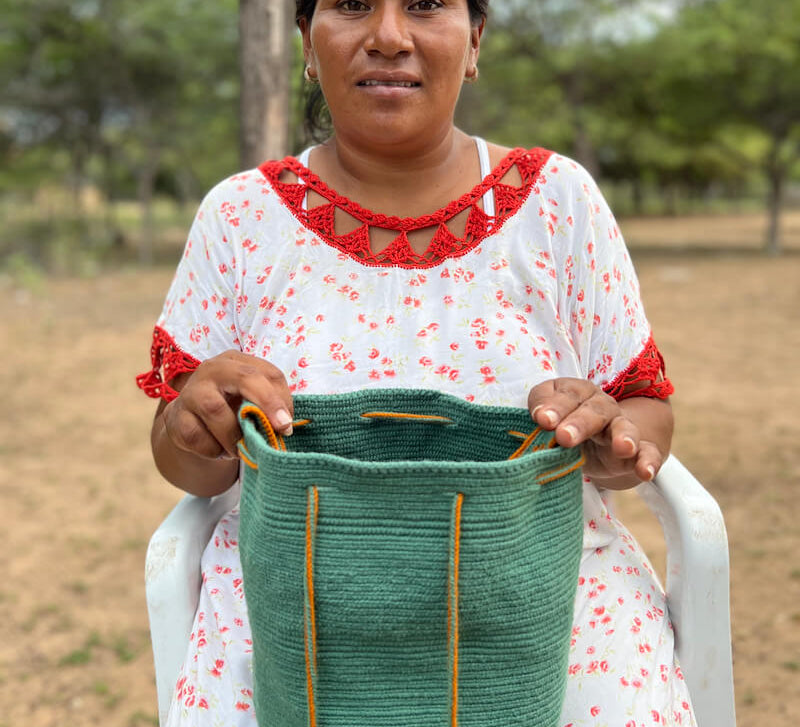 Wayuu woman holding a teal green crochet crossbody mochila